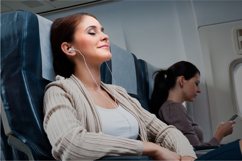 woman resting seated on an airplane, closing her eyes and wearing ear pods